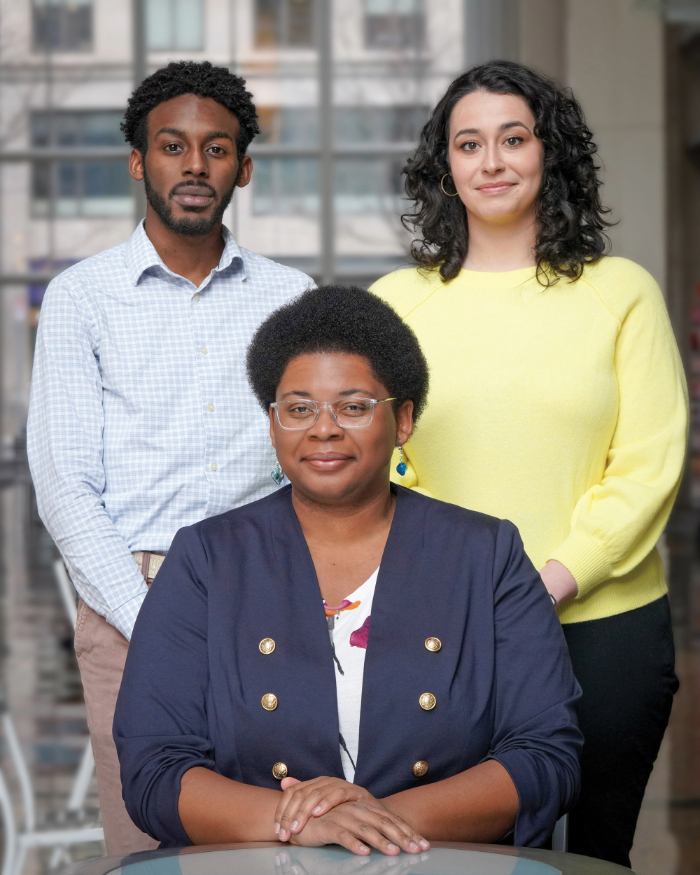 The TBF arts team - Dylan Mitchell, a young Black man with a short locks and a beard; Laura Reyes, a White woman with shoulder length dark hair, and Catherine Morris, a Black woman with glasses and with a short Afro, look toward the camera