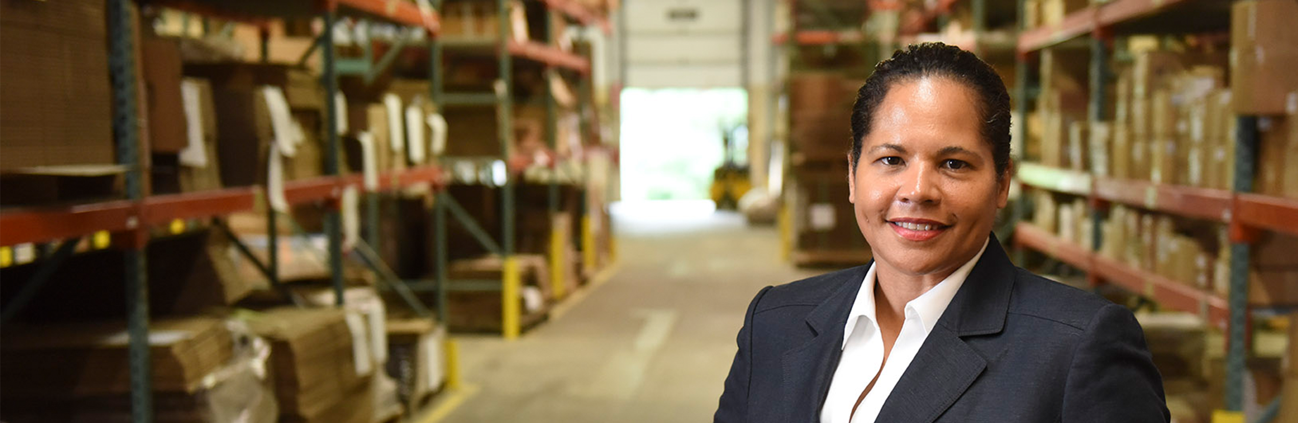 A woman stands in a warehouse in front of shelves filled with cardboard boxes