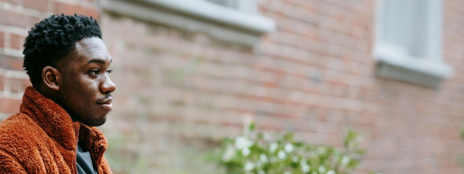 A profile photo of a young black man sitting on a bench in front of a brick building
