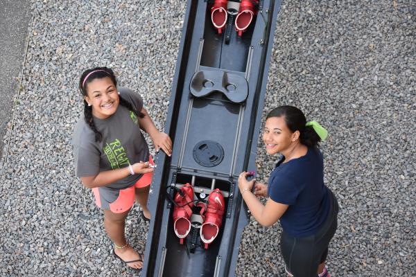 Two women stand on either side of a boat, they are posing for an aerial photo 