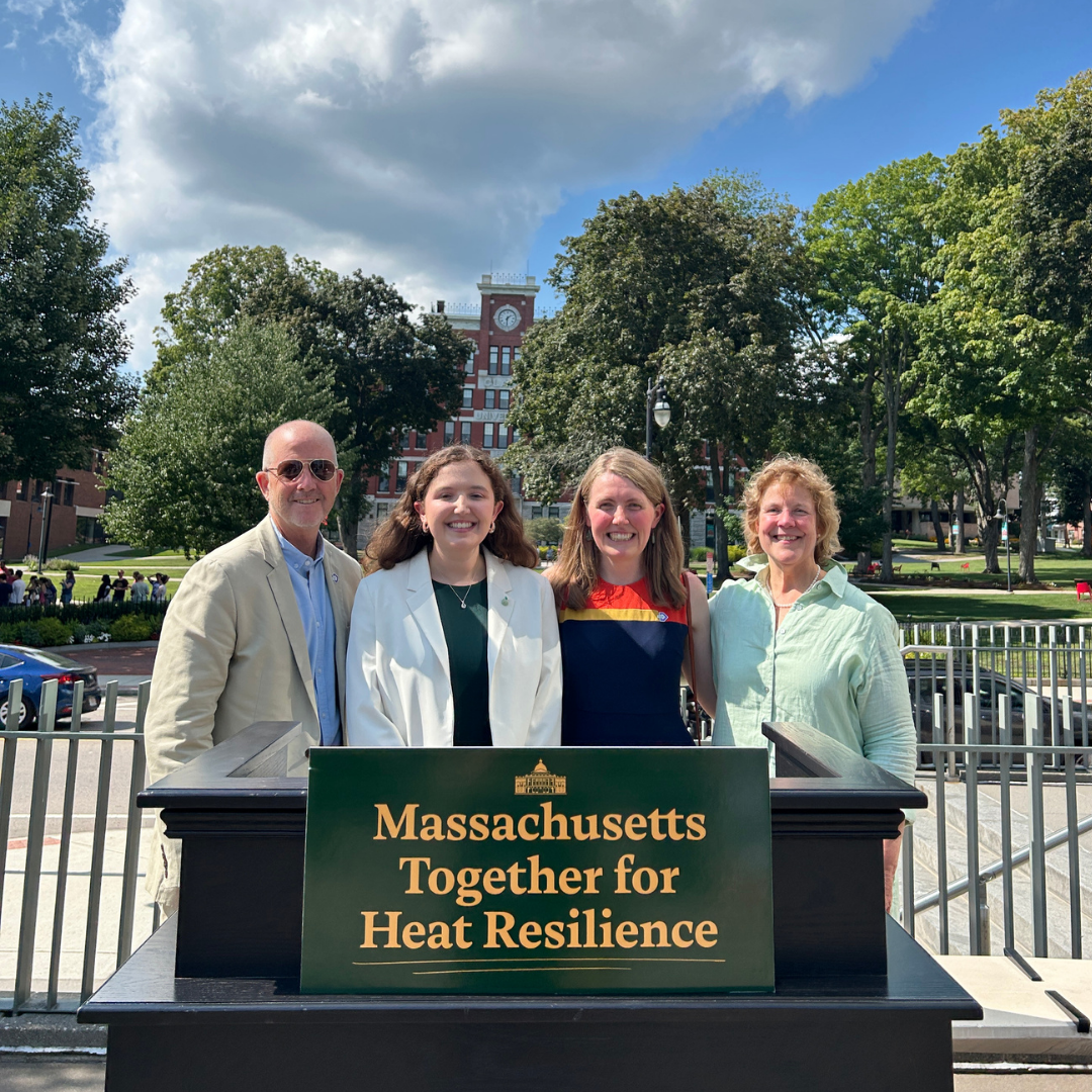 At an event at Clark University announcing the state's first heat resilience officer, four people pose behind a sign that says "Massachusetts Together for Heat Resilience." Group shot (left to right): Keith Mahoney (TBF), Katie Schlick (Heat Resilience Officer), Julia Howard (TBF), and Climate Chief Hoffer.