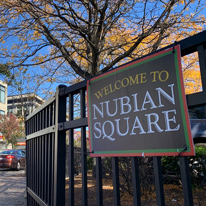 A sign hangs on a park fence, with text: Welcome to Nubian Square.