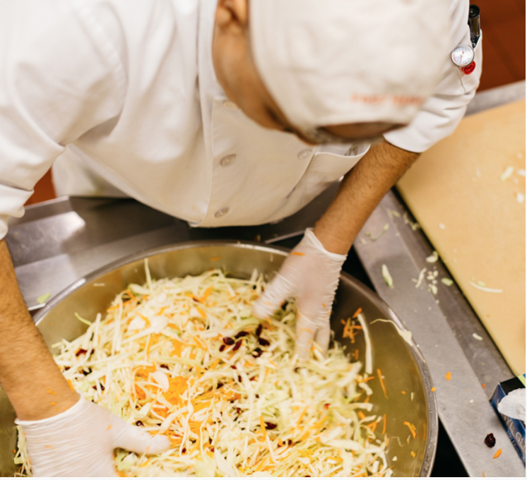 A man leaning over a van of food, stirring with his hands. Photo credit: Community Servings