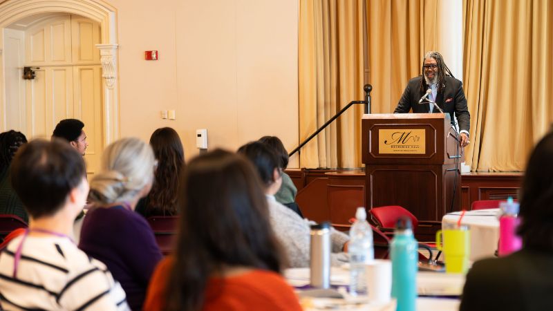 Dwaign Tyndal speaks from podium as seen from behind people at tables with colorful bottles.