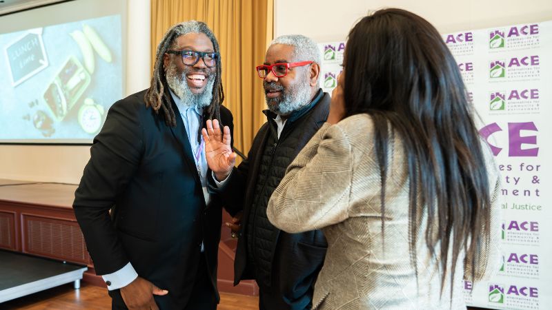 Dwaign Tyndal and a man with red glass talk with a woman whose back is to camera