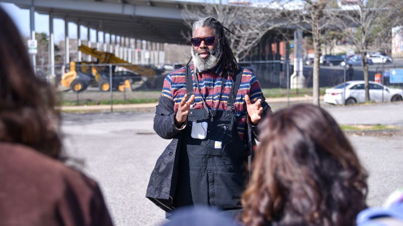 Dwaign Tyndal stands in a parking lot facing a group of people who are not seen in the photo.