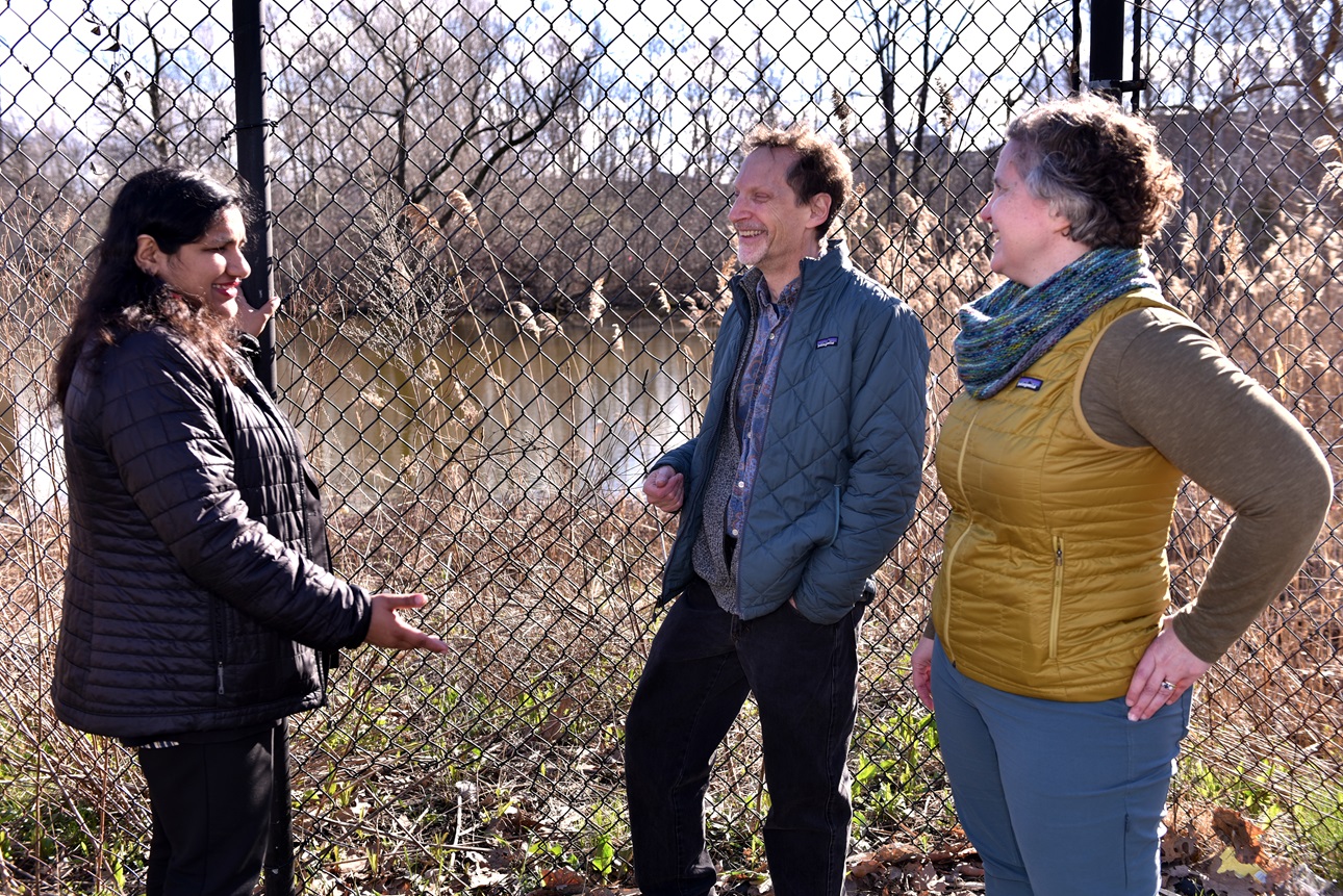 Cambridge Mayor Siddiqui, Grunebaum and Pomponi in discussion in front of fenced-in pond and brush.