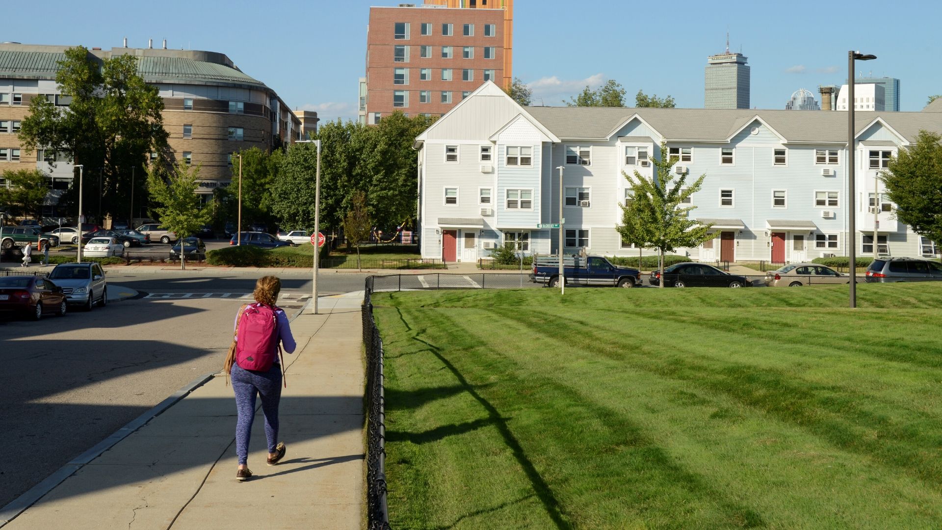 A blue condominium complex with green grass in the foreground, blue sky and an orange building in the background.