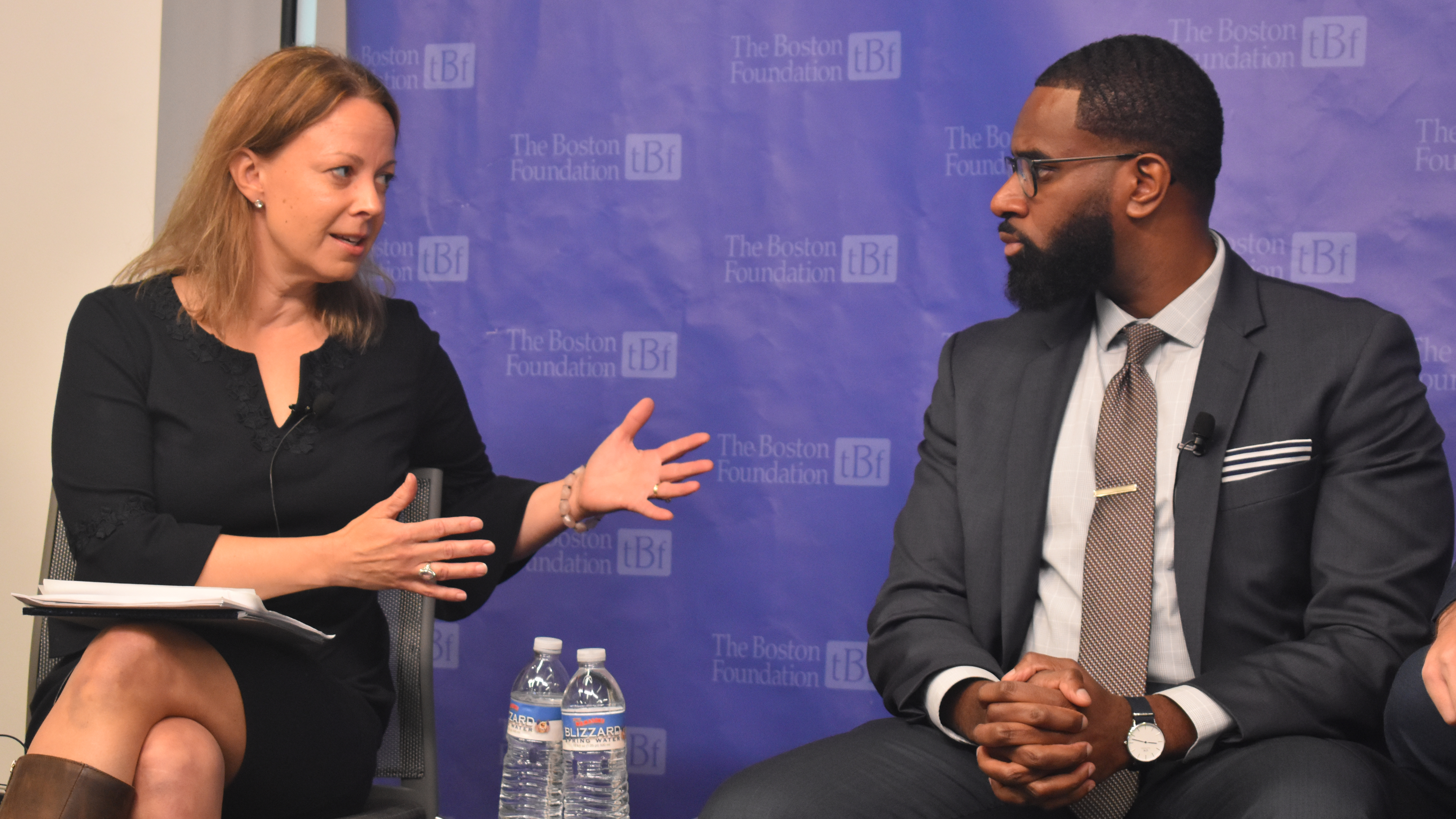 A woman and a man sit next to each other onstage, they are mid conversation.