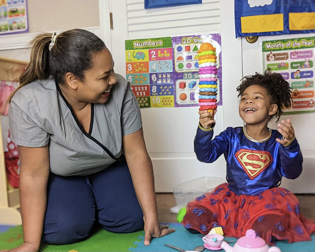 Child-care educator Romeyre Evangelista smiles at young girl with toy