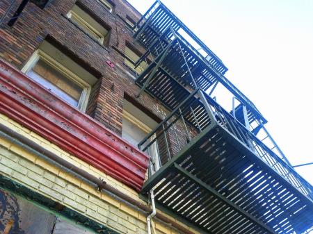An angled photo of the side of a multi-story brick building with a fire escape