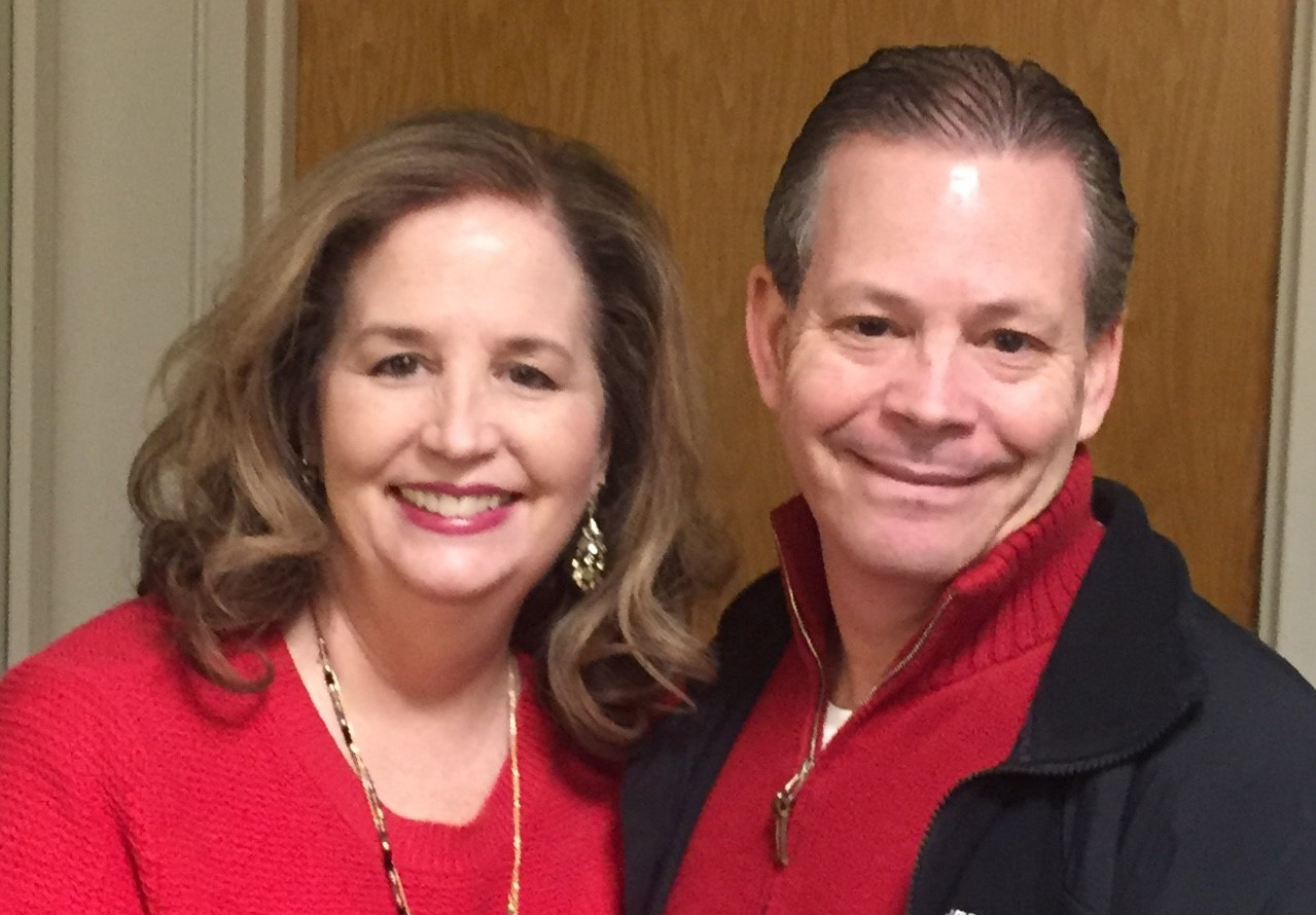 Mature darkhaired white wife and husband couple stand close and smile toward camera