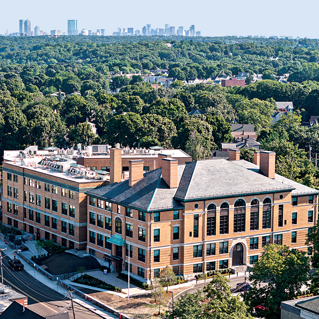 a drone photo of the Pryde building with trees in the background and the Boston skyline on the horizon.