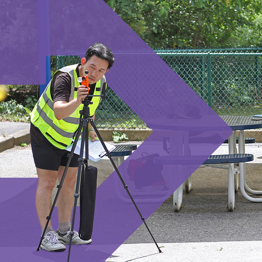 A man standing in a park next to picnic tables uses equipment on a tripod as part of the BCOOL data collection