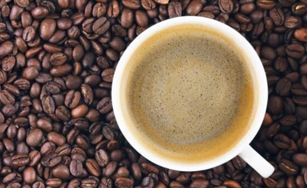 An overhead shot of white mug filled with coffee, sitting on a bed of coffee beans.
