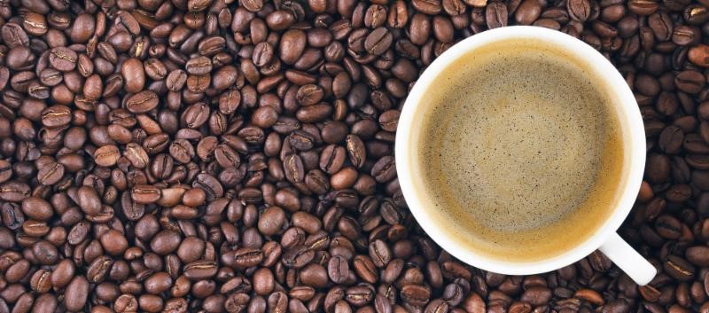 Overhead shot of a white mug full of coffee sitting on a bed of coffee beans.