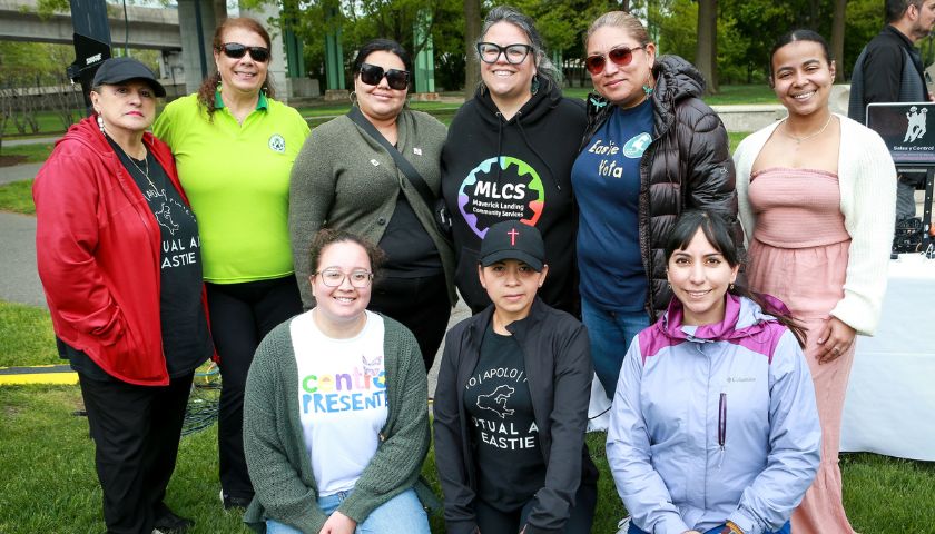 At the En Comunidad East Boston event, a group of partners stand and pose for a photo outside in a park