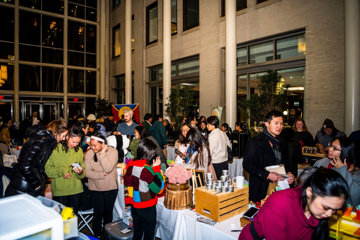 A photo in the atrium at the TBF office during the 2023 Shop AAPI holiday night market shows a large crowd of people shopping from tabled businesses selling merchandise.