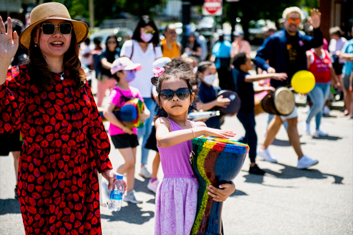 A woman and daughter march in the street during the 2022 Dorchester Day parade, the girl is carrying a colorful drum