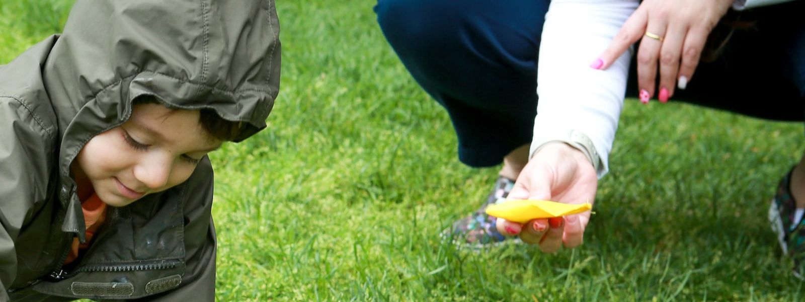 A toddler wearing a raincoat plays with yellow rings and bean bags in a grassy field