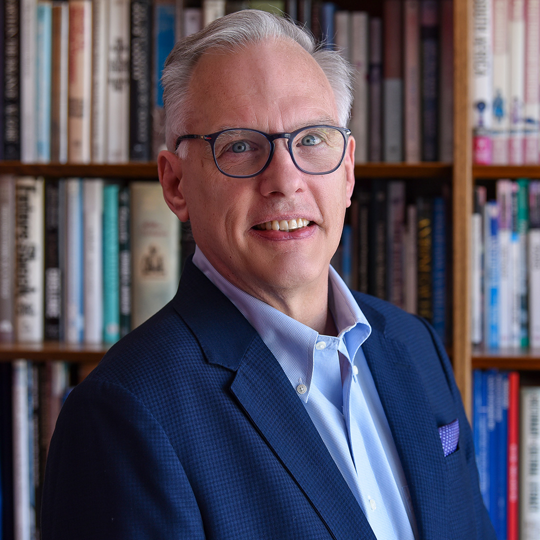 Dean Hara poses for a portrait photo with a bookcase behind him.