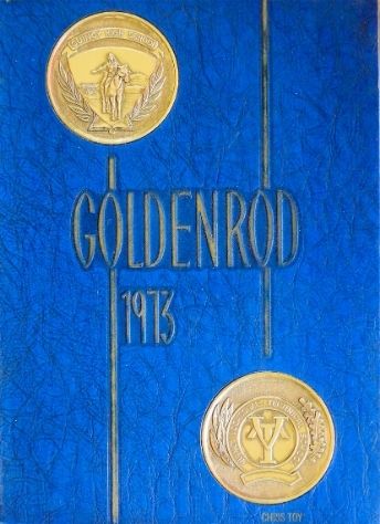 A yearbook cover; it's a rich blue color, with two golden seals on it - one on the top left and one on the bottom right. They have intricate designs of a man riding a horse with mountains behind him, and the Quincy Vocational Tech. High logo. Two golden lines run from the seals, up/down the length of the cover. Golden text in the middle says "Goldenrod, 1973."