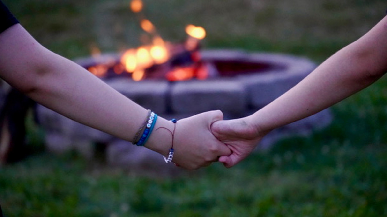 Two kids hold hands at a campfire