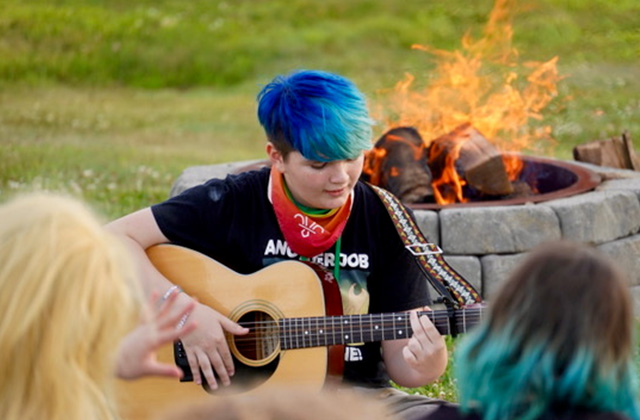 A camper plays guitar at a firepit