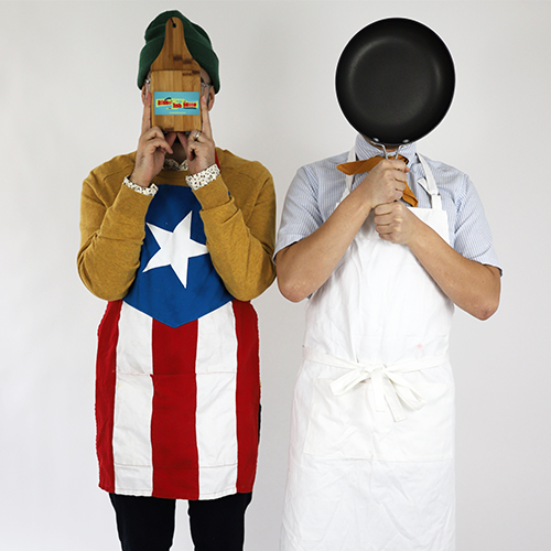 Two members of Adobo Fish Sauce are standing and covering their faces with a cutting board and frying pan