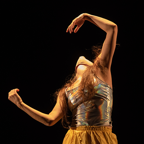 A person photographed while dancing, their arms are outstretched and bent at the elbows and their head is thrown back.