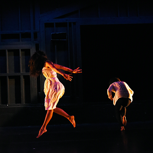 Two people are on a dark stage dancing, only their silhouettes can be seen