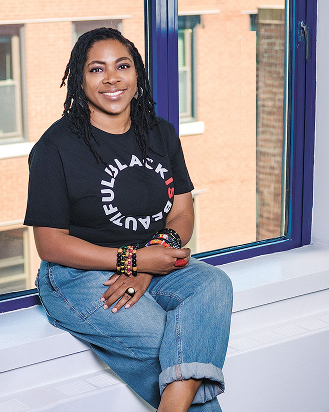 Nickey Nesbeth sits on a windowsill inside smiling for a photo