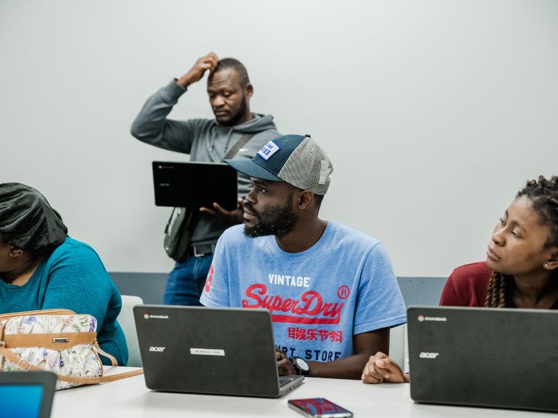 BRICC computer training day at the YMCA. A classroom or training room with several people seated at tables working on laptops. The atmosphere suggests a hands-on workshop or computer-based learning session.