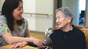 An elderly Asian woman sits with a younger Asian woman at a table indoors.