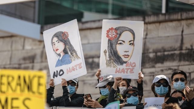 A crowd of people in protest. Two signs are being held up with Asian women drawn on them, with the words "no hate" and "stop Asian hate" written on them.