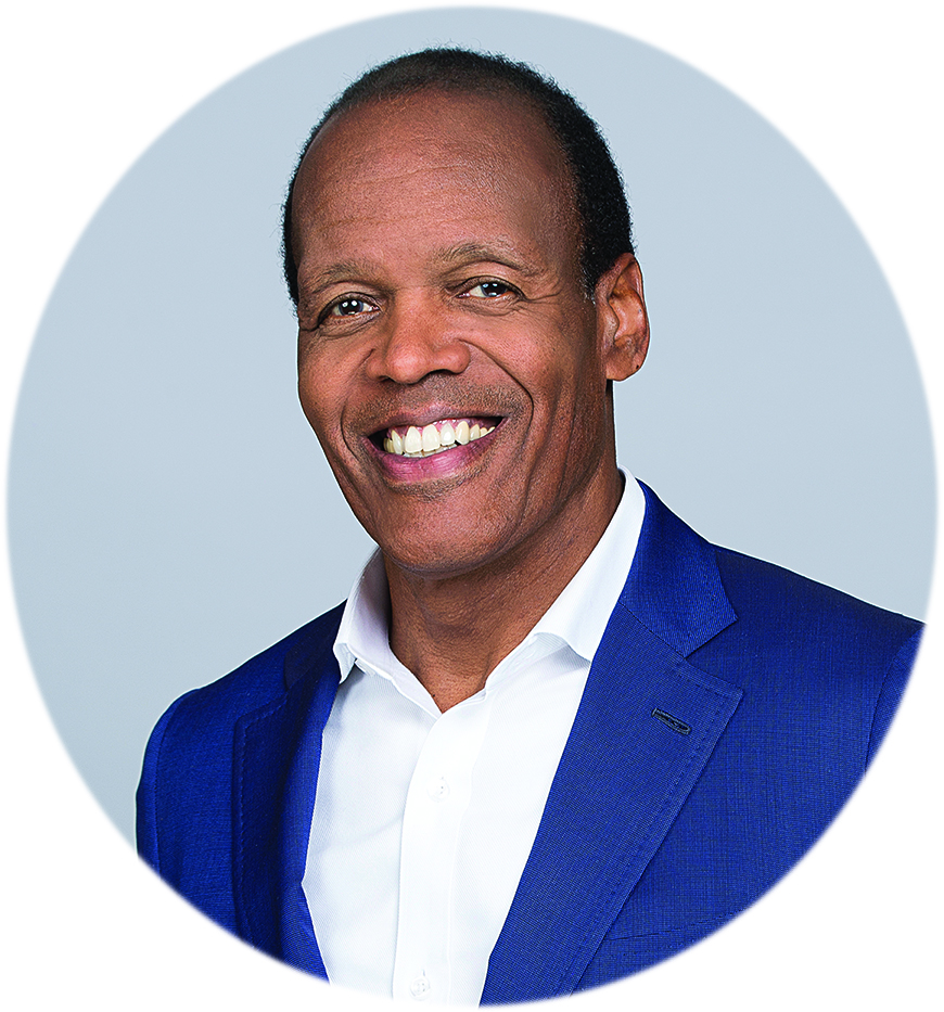 A circular headshot of Lee Pelton. He's wearing a dark blue blazer and a white collared shirt, standing against a gray background.