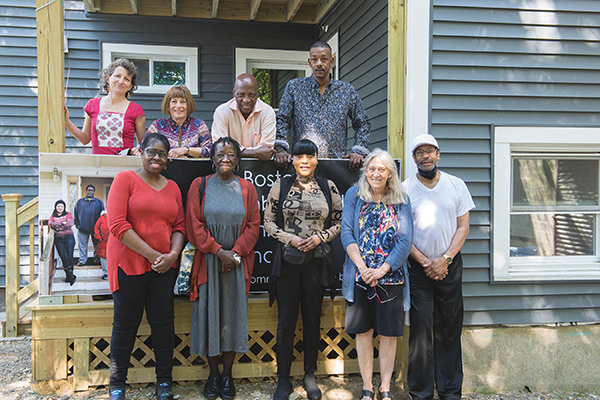 A group of men and women pose for a photo in front of a house to celebrate acquiring the property for affordable housing
