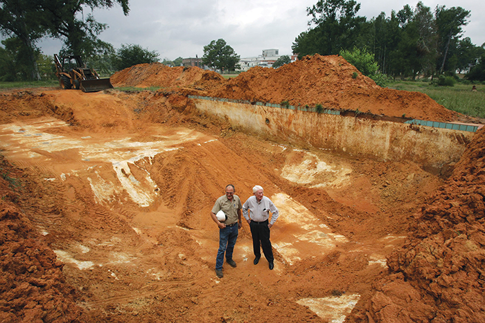 Two men stand in a pit of dirt, the site of a swimming pool in Stonewall, Mississippi that was filled in with truckloads of red dirt in the 1970s and is now being revived