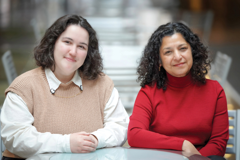 The TBF housing team: Helen Murphy, a white woman in a tan sweater vest, and Soni Gupta, an Indian woman in a red turtleneck, sits at a table in an atrium