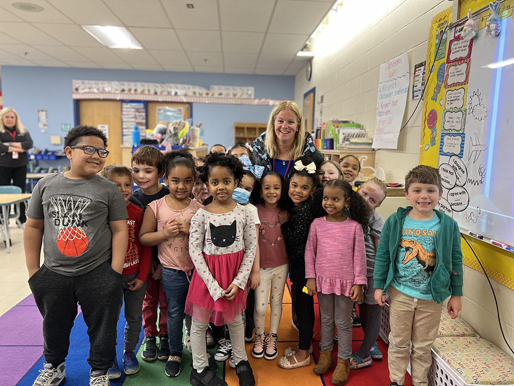 A group of elementary school students stand in a classroom and pose for a photo with the school Principal
