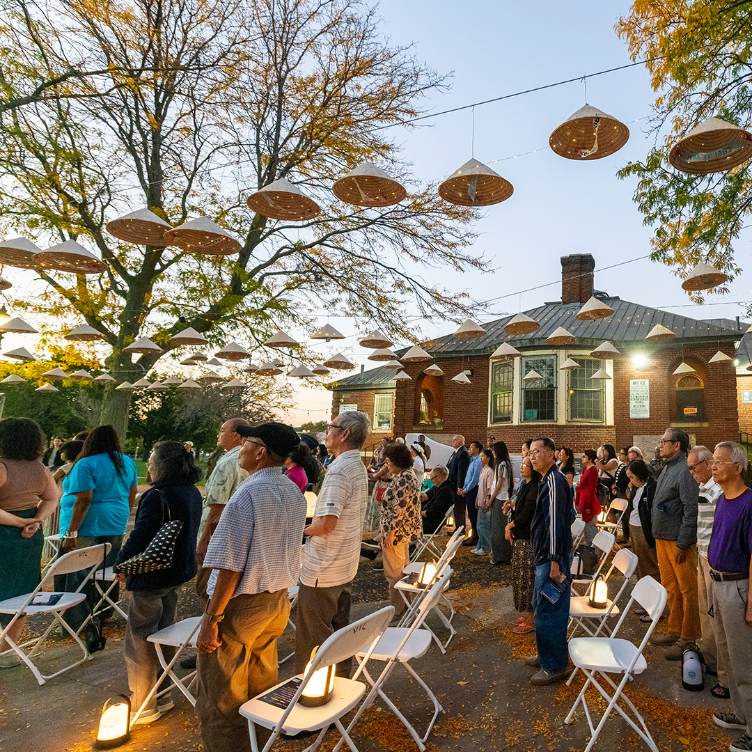 People gather outside under decorative outdoor lighting just before sunset