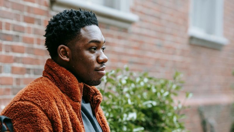 A profile photo of a young black man sitting on a bench in front of a brick building