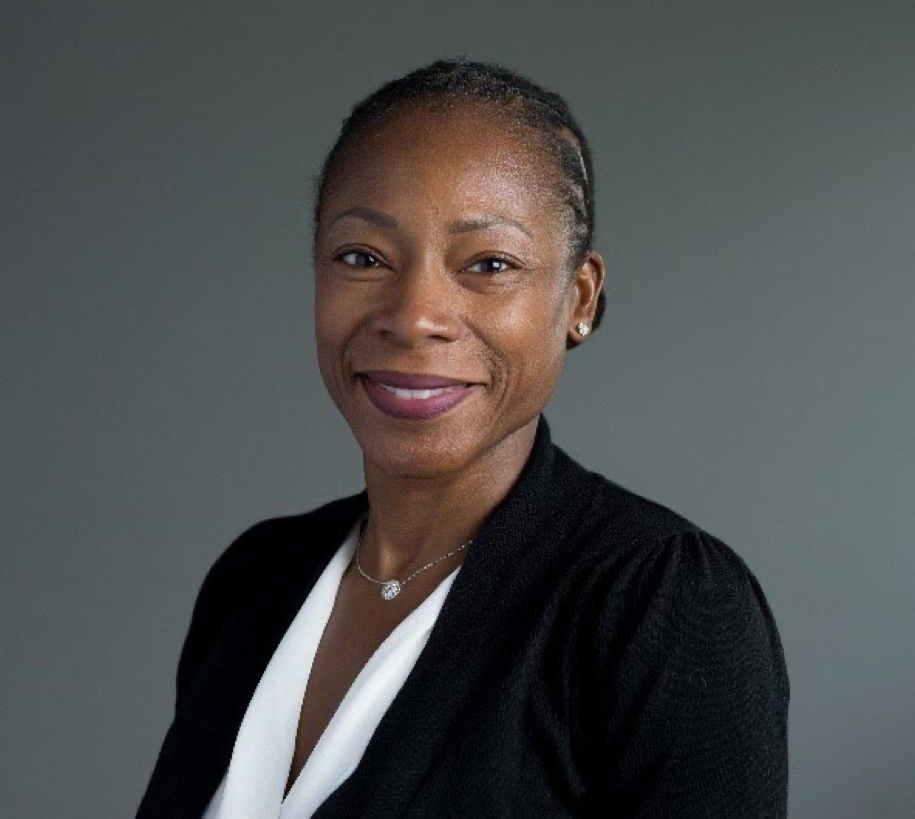 Headshot of Dr. Myechia Minter-Jordan. She's smiling, wearing a black blakers and a white blouse, and her hair is in an up do. The background is gray.
