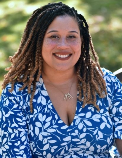Headshot of Jade Franco. She's wearing a white and blue shirt and has her hair styled in locs. 