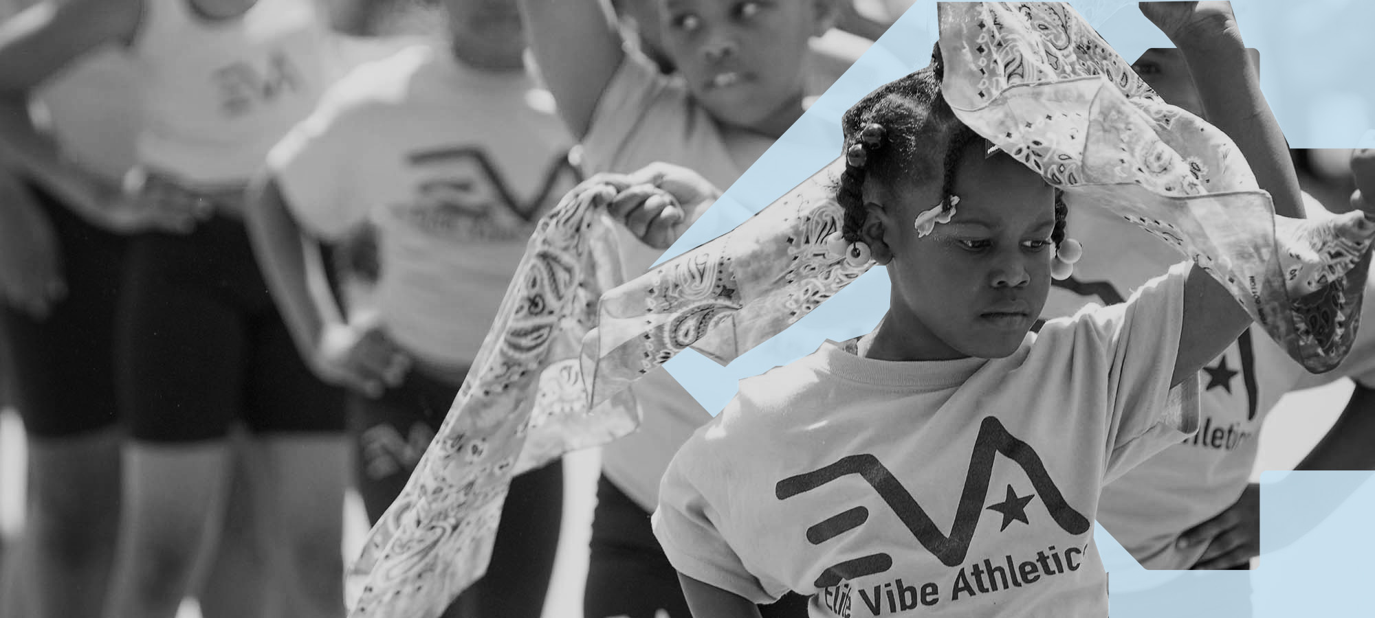 A girl dances in a parade twirling a scarf above her head. In the background is the blue TBF arrow