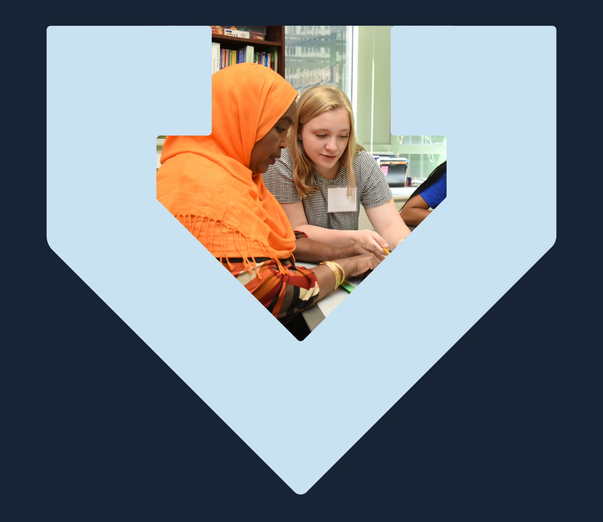 A volunteer sits with a woman wearing a headscarf teaching her English, the photo is framed by the light blue TBF arrow